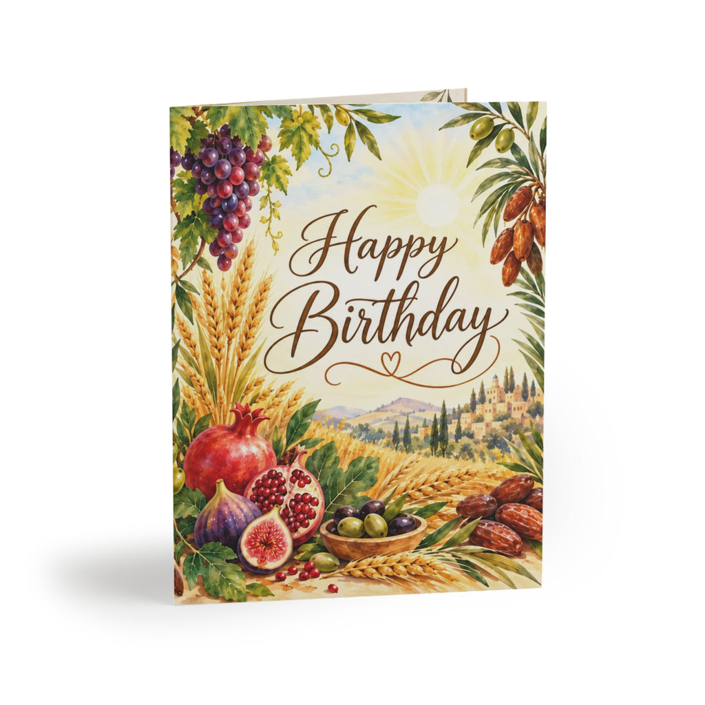 A vertical birthday greeting card featuring an illustrated harvest scene with wheat stalks, grapes, pomegranates, olives, dates, and a bright sun over a landscape. The words 'Happy Birthday' are printed in large brown script across the center.