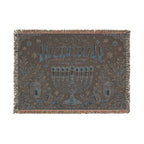 A rectangular woven throw blanket with fringe on all sides, featuring a dark brown background with a blue and beige menorah, stars, floral motifs, and Hebrew text reading 'Shin L'Chaim' on a white background.