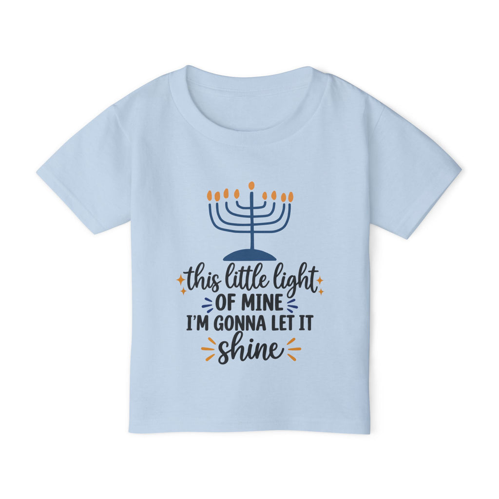A light blue short-sleeve kids' t-shirt with a Hanukkah graphic on the front. The graphic features a navy blue menorah with orange flames and the text 'this little light OF MINE I'M GONNA LET IT shine' in navy and orange lettering.