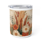A white insulated tumbler with a clear lid, featuring a printed autumn floral design with orange and cream flowers, beige pampas grass, and Bible verse text on a warm beige background.