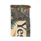 A folded woven throw blanket with fringed edges, featuring a multicolor mosaic pattern with a large dark navy letter 'Y' on a beige background and a tree motif. The underside shows a brown plaid pattern.