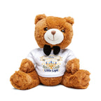 A brown plush teddy bear sitting on a white background, wearing a white T-shirt with a black bow tie and a Hanukkah 'Olivia Little Light' graphic on the front.