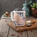 A white insulated coffee mug with a floral print and Bible verse, displayed on a wooden cutting board with coffee beans, sugar cubes, and a spoon in a kitchen setting.