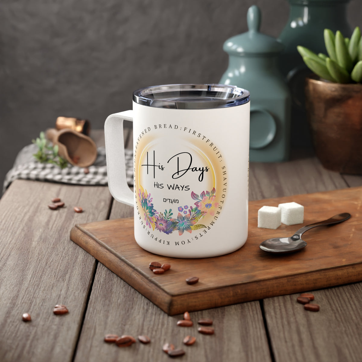 A white stainless steel mug with a floral graphic and the text 'His Days His WAYS around' sits on a wooden cutting board on a rustic table, styled with coffee beans, sugar cubes, a spoon, and a teal teapot in the background.