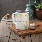 A white stainless steel insulated mug with a floral watercolor design and the word 'Shalom' printed on the side, styled on a wooden cutting board with coffee beans, sugar cubes, and a spoon in a kitchen setting.
