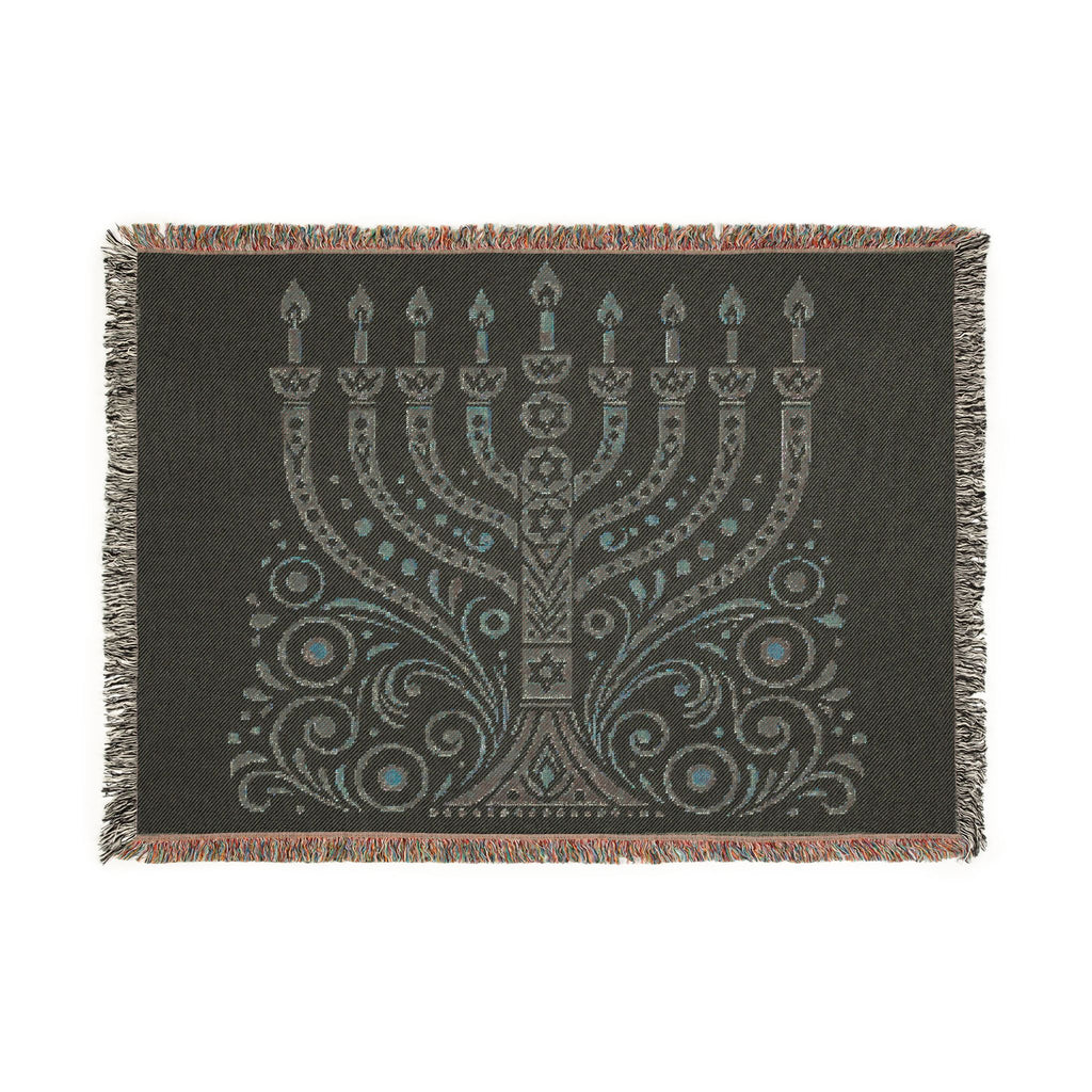 A rectangular woven throw blanket with fringe on all sides, featuring a large menorah and ornate scrollwork design in light gray and turquoise on a dark charcoal background.