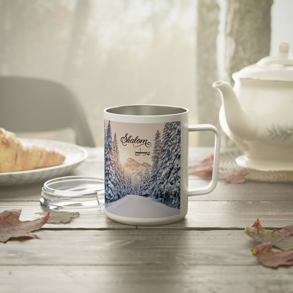 A white stainless steel mug with a custom printed winter forest design and the name 'Slaton' on the front, set on a rustic wooden table with a glass lid, a teapot, and autumn leaves in a cozy, softly lit environment.