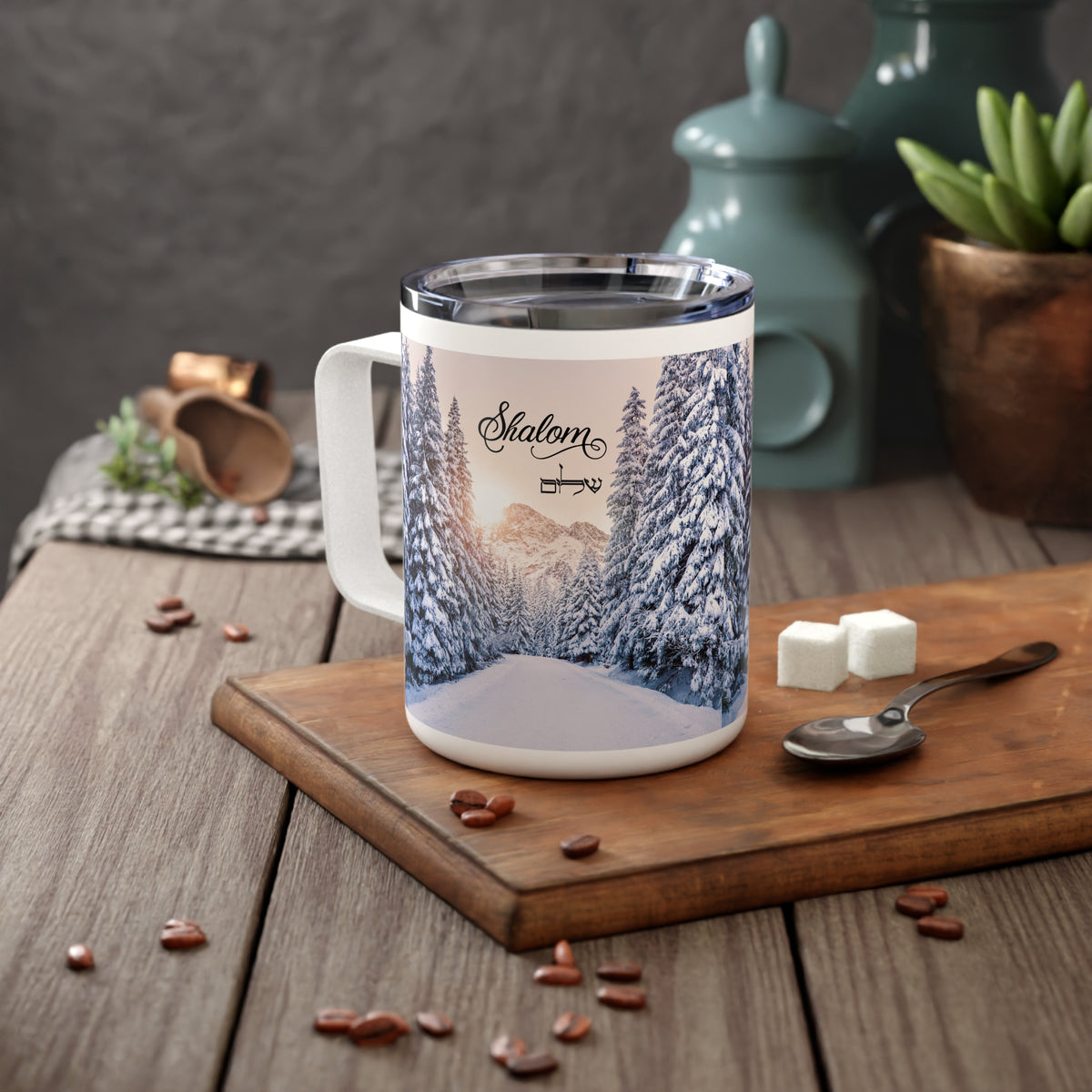A white stainless steel coffee mug with a printed winter forest scene and the word 'SkateLM' on the side, placed on a wooden cutting board with coffee beans, sugar cubes, and a spoon in a kitchen setting.