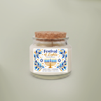 A white soy wax candle in a clear glass jar with a cork lid, featuring a decorative label that reads 'Festival of Lights - Hanukkah' with blue and gold illustrations, set against a solid light sage green background.