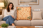 A woman sits on a beige sofa next to a large decorative pillow with a matzah bread crust pattern and green leaf accents. White measurement labels indicate the pillow's dimensions: XL - 27.