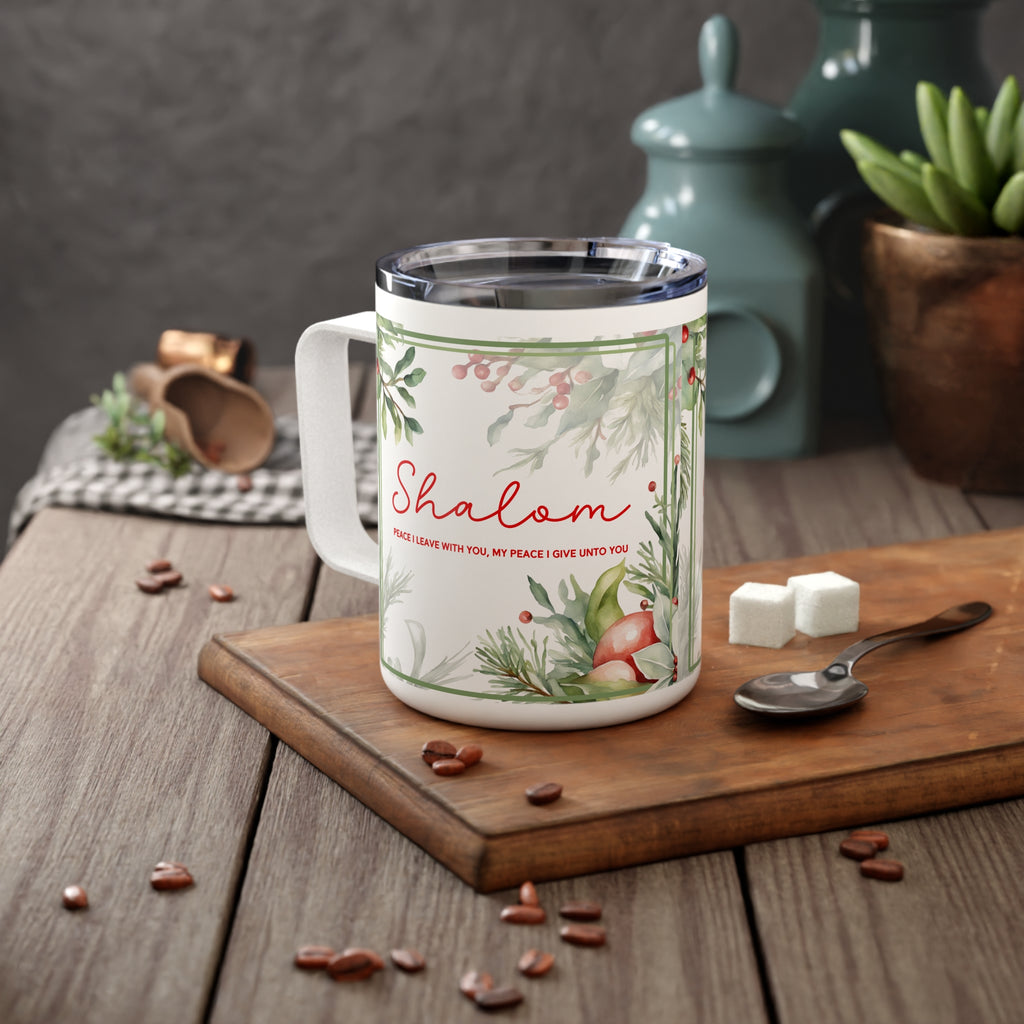 A white stainless steel  mug with a clear lid sits on a wooden cutting board in a kitchen setting. The mug features a festive winter design with green pine branches, red berries, a fox, and the word 'Shalom' in red script, along with a small quote.