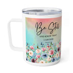 A white stainless steel travel mug with a clear lid, featuring a colorful floral design and the text 'Be Still AND KNOW THAT I AM GOD PSALM 40:1' on the front, set against a plain white background.