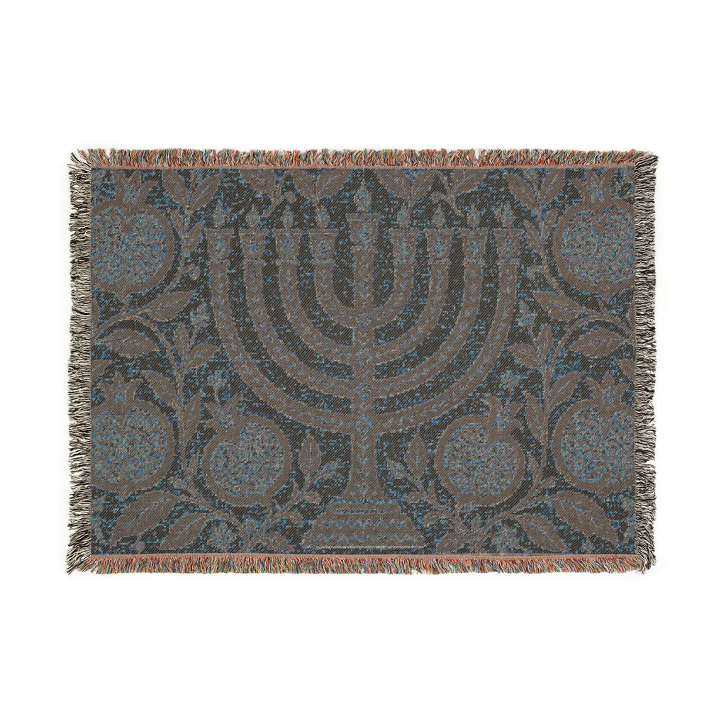 A rectangular woven throw blanket featuring a central menorah motif with pomegranate and floral patterns, finished with fringed edges in a muted blue, gray, and brown palette.
