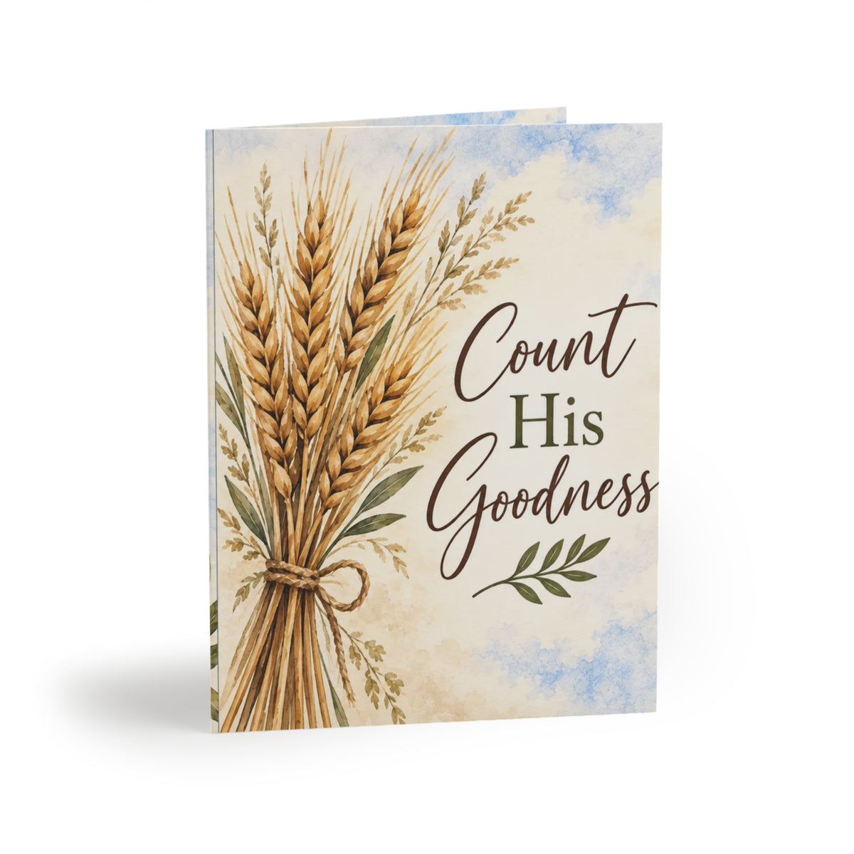 A greeting card featuring an illustration of a tied bundle of golden wheat stalks on a cream watercolor background with blue sky accents. The text 'Count His Goodness' is printed on the front.