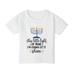 A white short-sleeve kids' t-shirt with a Hanukkah graphic on the front. The graphic features a blue menorah with orange flames and the text 'this little light OF MINE I'M GONNA LET IT shine' in dark blue and orange cursive fonts.
