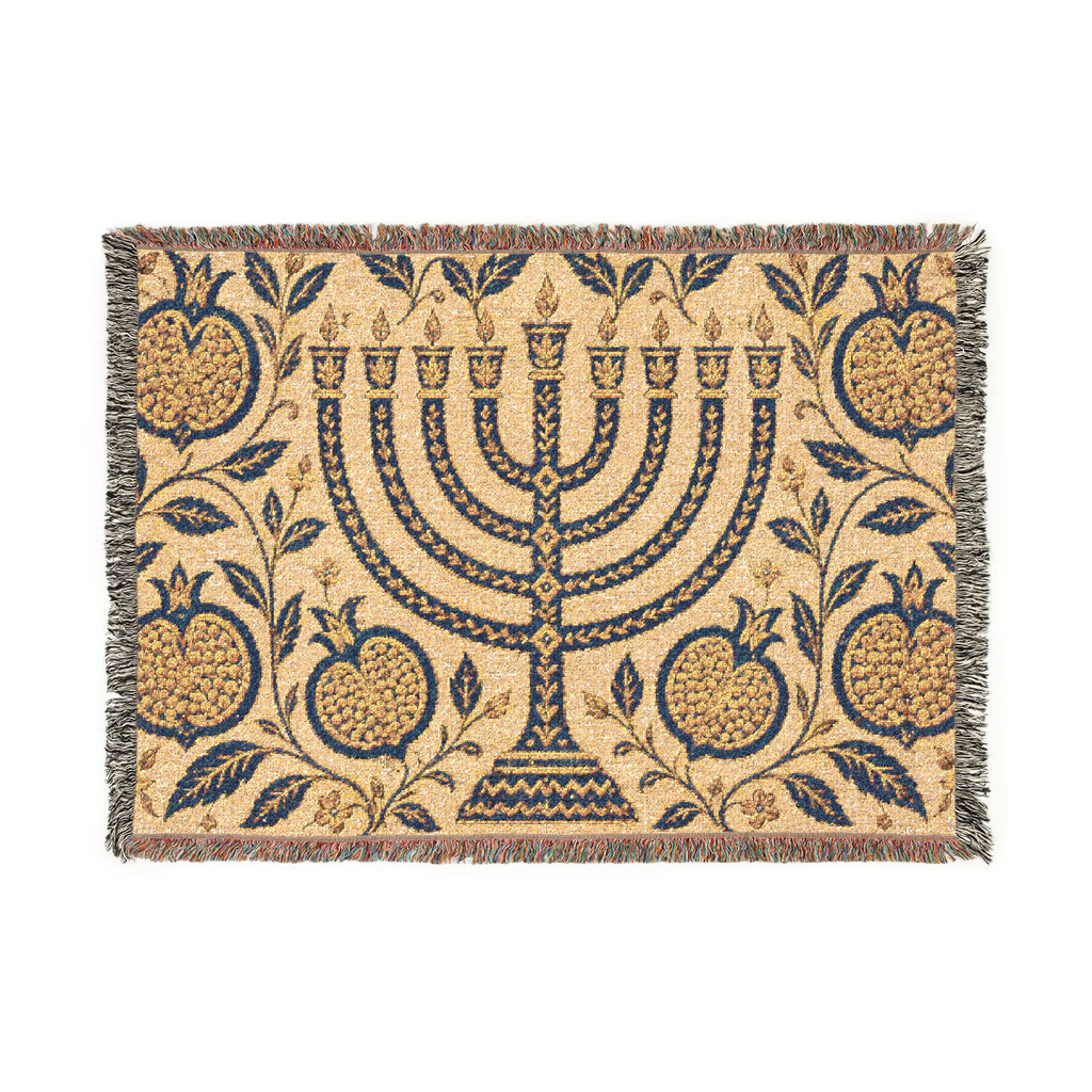 A rectangular woven textile with fringe on all sides, featuring a central menorah surrounded by pomegranate and leaf motifs. The design is primarily navy blue on a warm beige background.