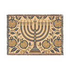 A rectangular woven textile with fringe on all sides, featuring a central menorah surrounded by pomegranate and leaf motifs. The design is primarily navy blue on a warm beige background.