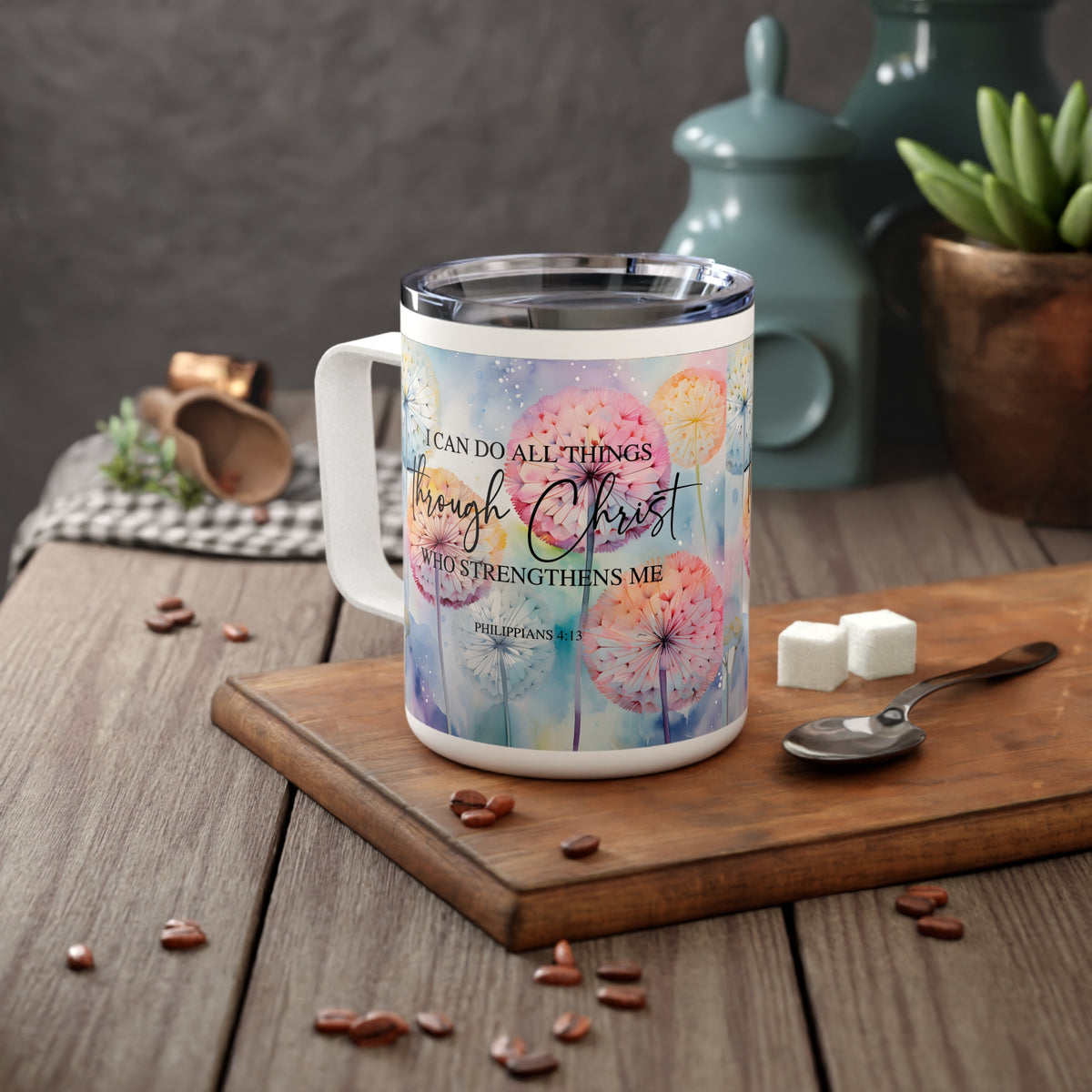 A white stainless steel mug with a colorful watercolor dandelion design and the Bible verse 'I CAN DO ALL THINGS through Christ WHO STRENGTHENS ME' (Philippians 4:13), shown on a wooden cutting board in a styled kitchen setting.