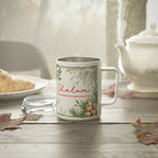 A white stainless steel  mug with a silver interior, featuring a green botanical border and the word 'Shalom' in red script, set on a rustic wooden table with a glass lid, a teapot, and autumn leaves in the background.