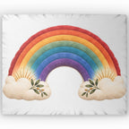 A square white pillow or cushion featuring a large colorful rainbow design with cream clouds at the bottom and small green leafy sprigs.