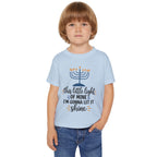A young child wearing a light blue graphic t-shirt with a Hanukkah menorah and the text 'this little light OF MINE I'M GONNA LET IT shine' printed on the front, paired with blue jeans, set against a plain white background.