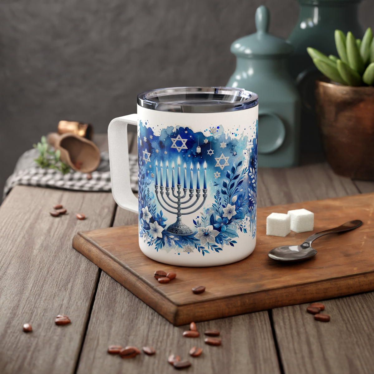 A white stainless steel -style mug with a blue Hanukkah menorah and floral design, set on a wooden cutting board with coffee beans, sugar cubes, and a spoon on a rustic table.