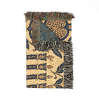 A woven throw blanket with a cream base and navy blue, teal, and brown geometric and floral patterns, featuring fringed edges.