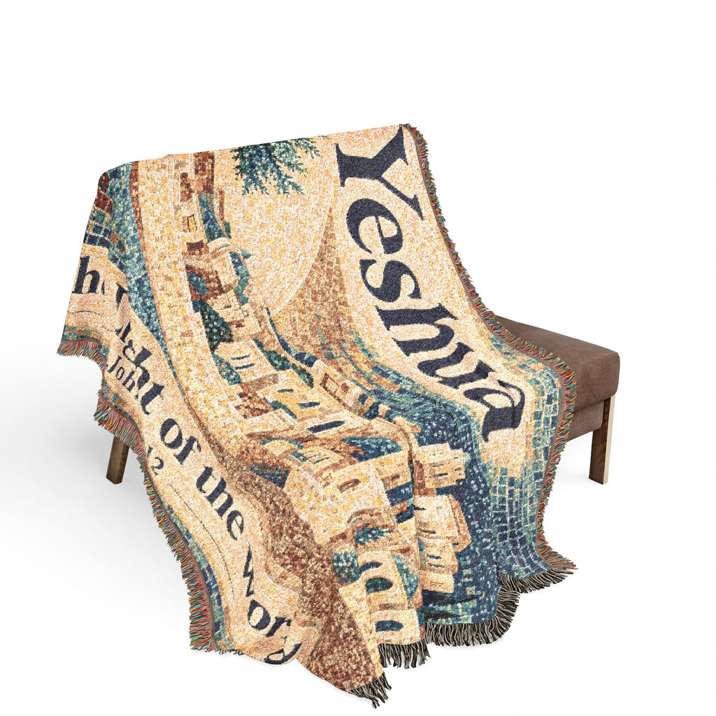 A woven throw blanket with fringe, draped over a brown bench against a plain white background. The blanket features a detailed tapestry-style design with the word 'Yeshua' in large dark blue letters, along with architectural imagery and additional text.