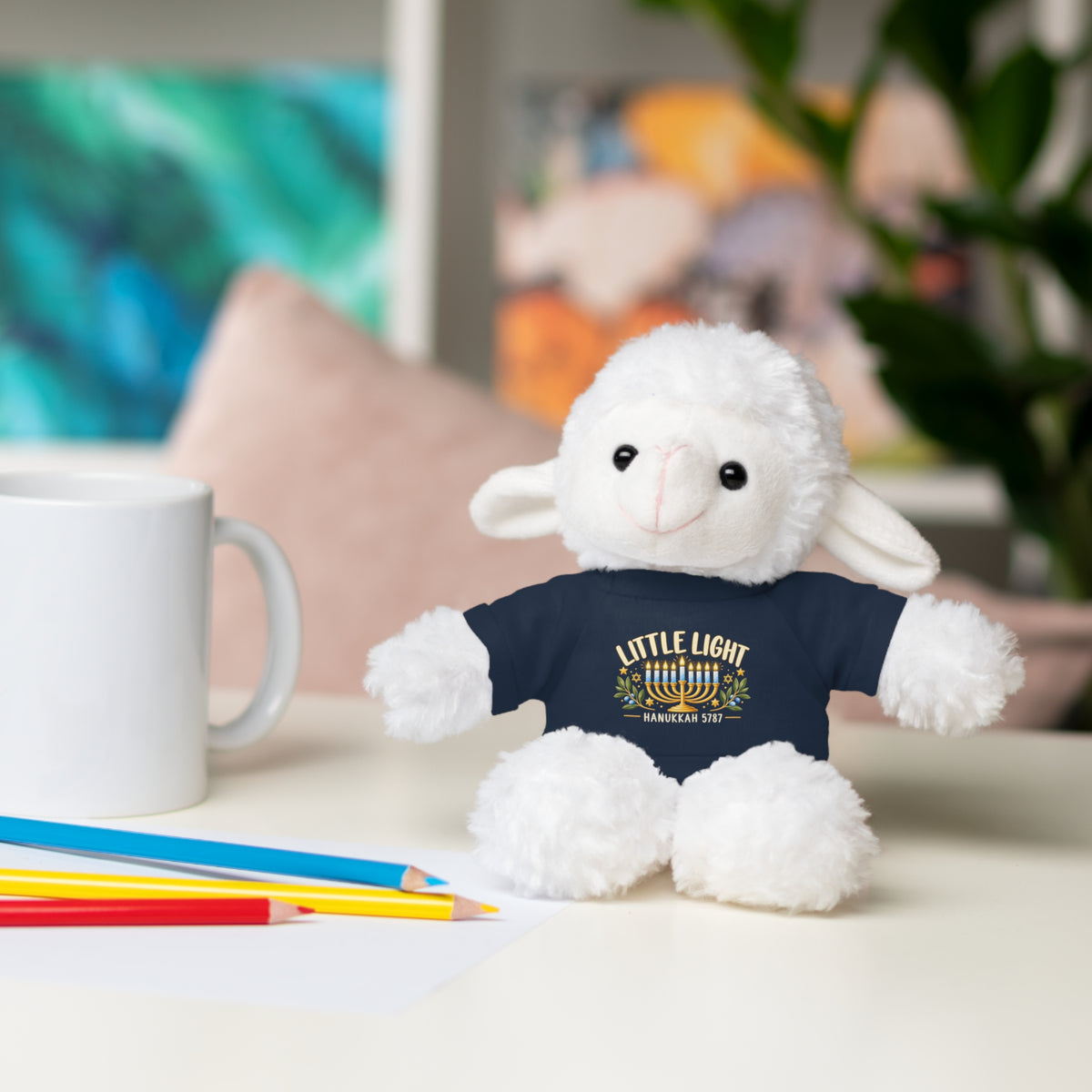 Stuffed animal wearing a green shirt with a design, sitting on a table with a mug and pencils.