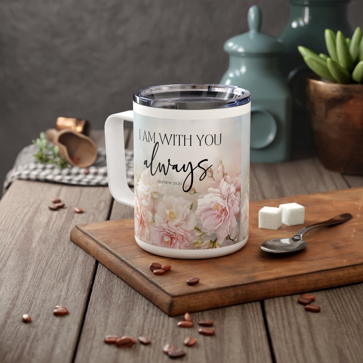 A white stainless steel  mug with a clear lid sits on a wooden cutting board on a rustic wooden table. The mug features a floral print with the text 'I AM WITH YOU always' in black script and serif fonts.