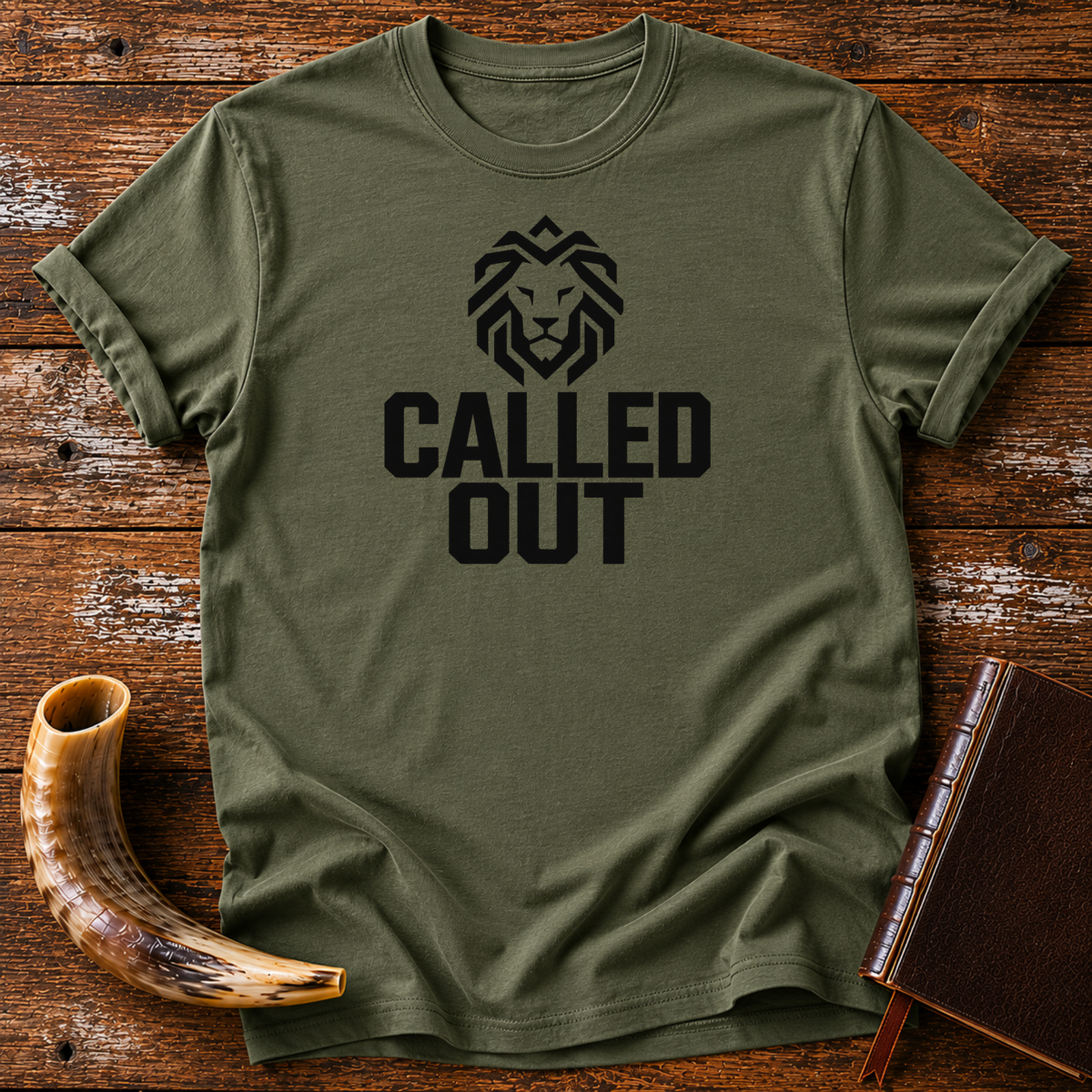 Military green t-shirt with a geometric black lion head over bold CALLED OUT text, laid flat with a shofar and a leather book