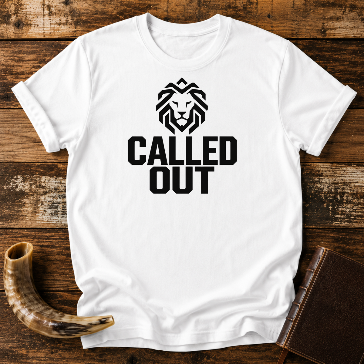White t-shirt with a geometric black lion head over bold CALLED OUT text, laid flat with a shofar and a leather book