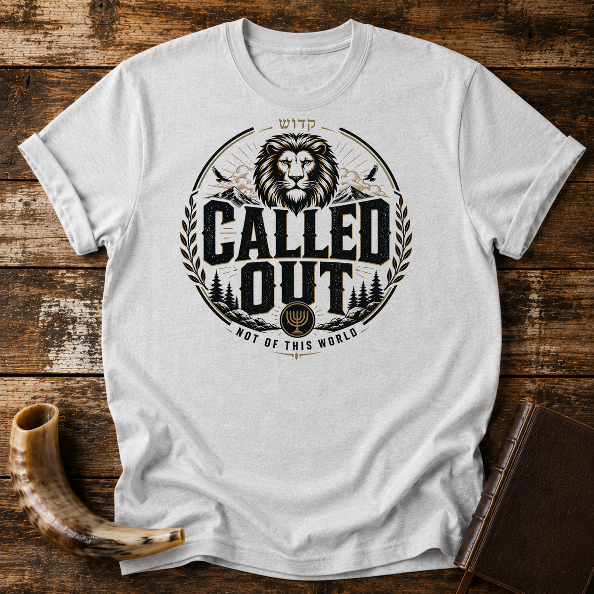 Sport grey t-shirt with a CALLED OUT lion badge with Hebrew lettering, a menorah and NOT OF THIS WORLD, laid flat with a shofar and a leather book