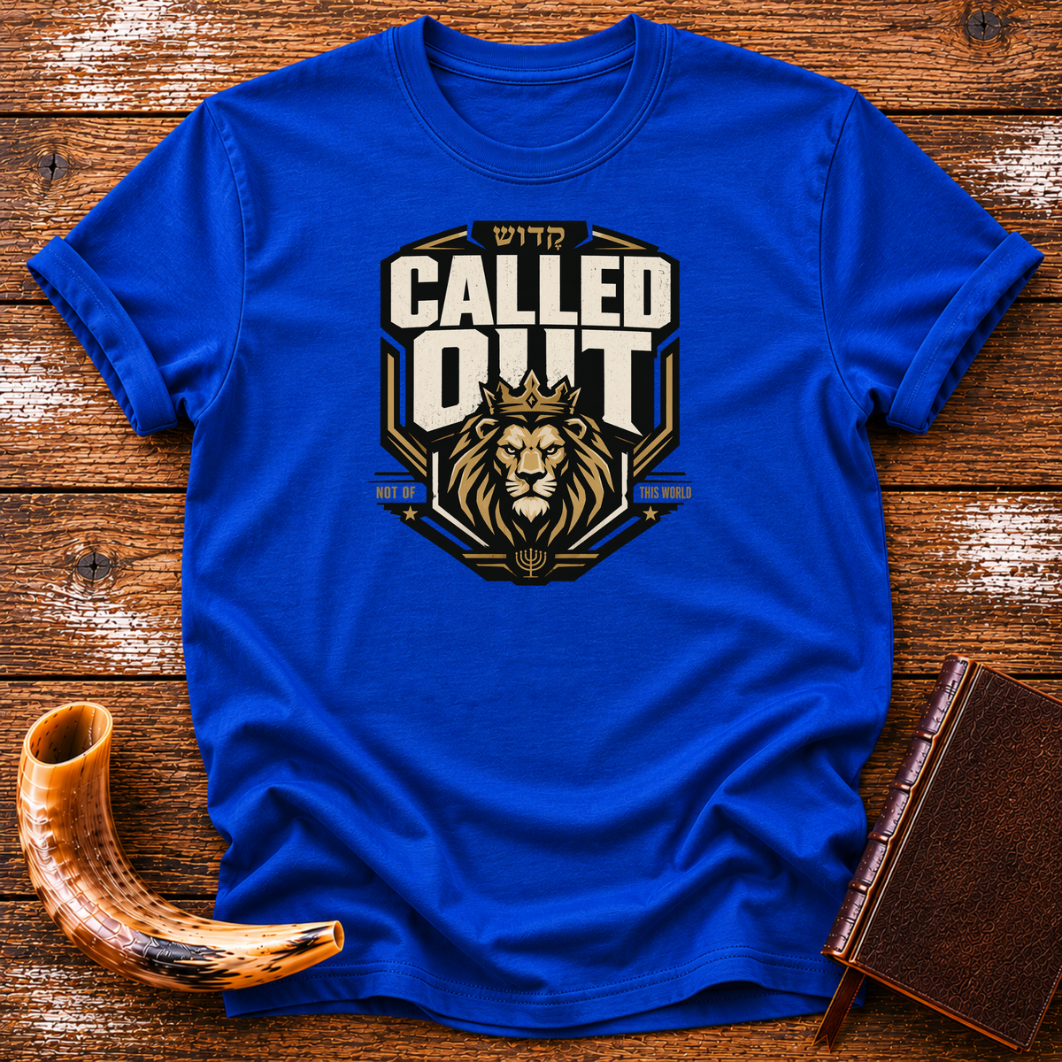 Royal blue Called Out tee with a crowned lion badge and Hebrew lettering, laid flat with a shofar and a leather-bound book