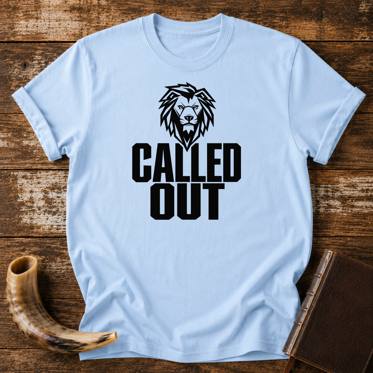 Light blue t-shirt with a black lion head above bold CALLED OUT text, laid flat with a shofar and a leather book