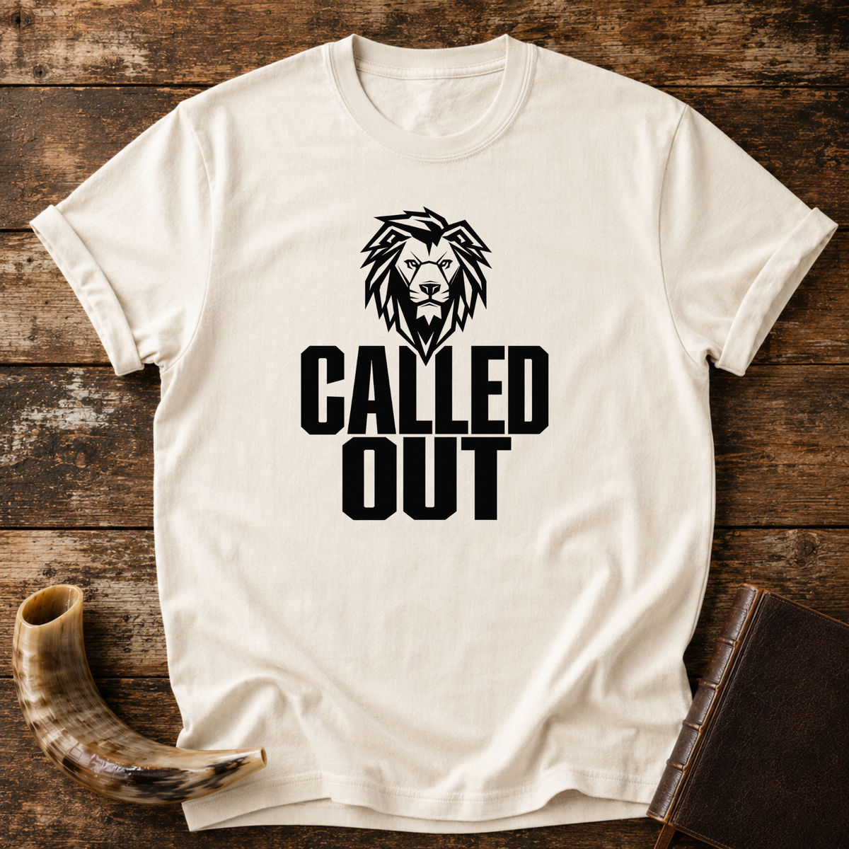 Natural cream t-shirt with a black lion head above bold CALLED OUT text, laid flat with a shofar and a leather book