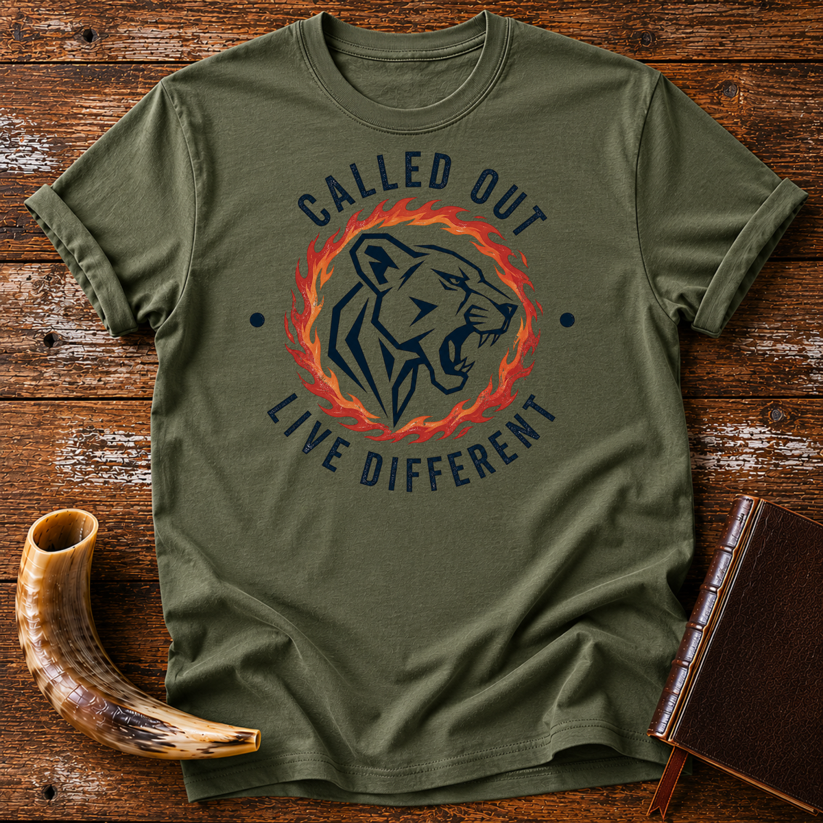 Military green t-shirt with a roaring lioness in a ring of fire with CALLED OUT and LIVE DIFFERENT, laid flat with a shofar and a leather book