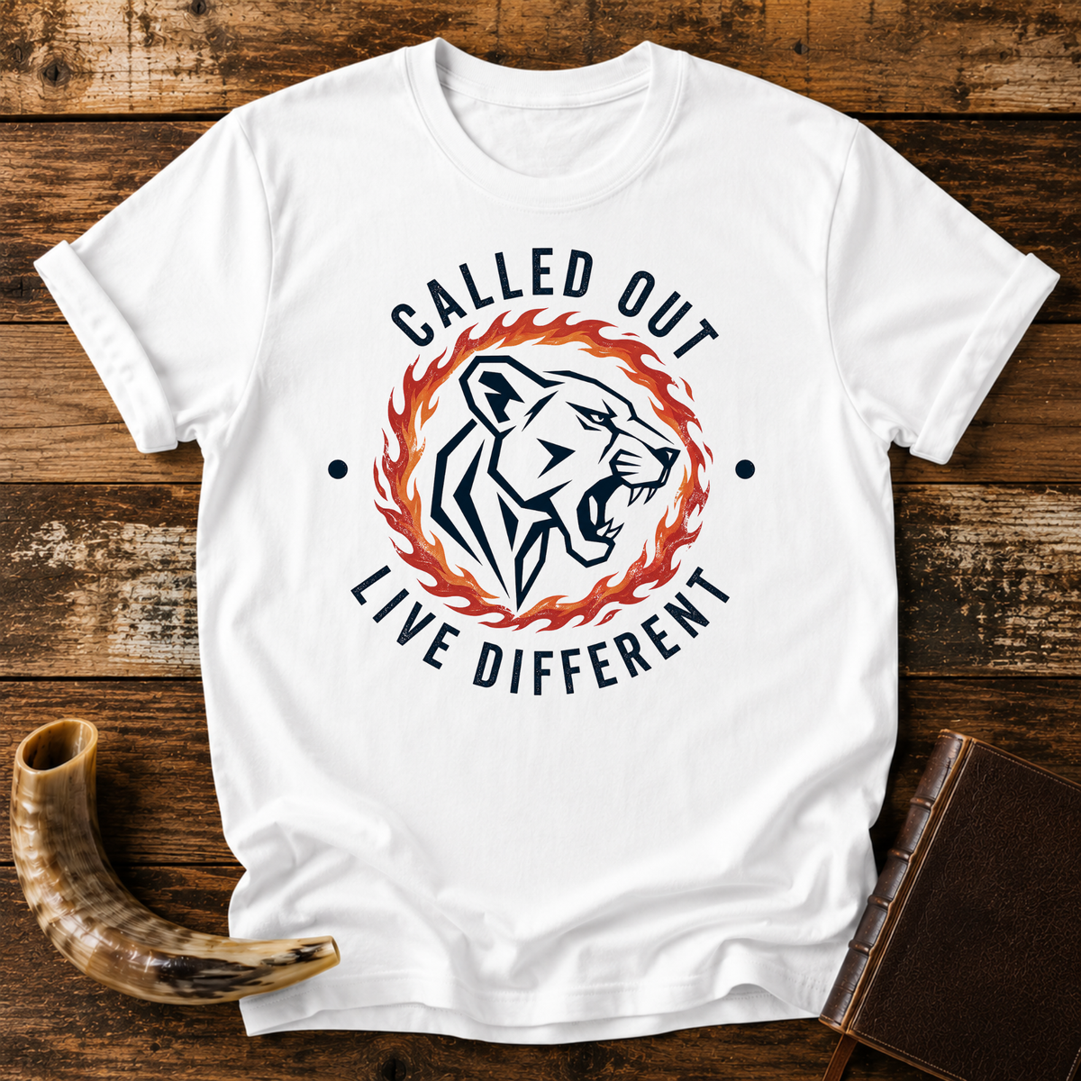 White t-shirt with a roaring lioness in a ring of fire with CALLED OUT and LIVE DIFFERENT, laid flat with a shofar and a leather book