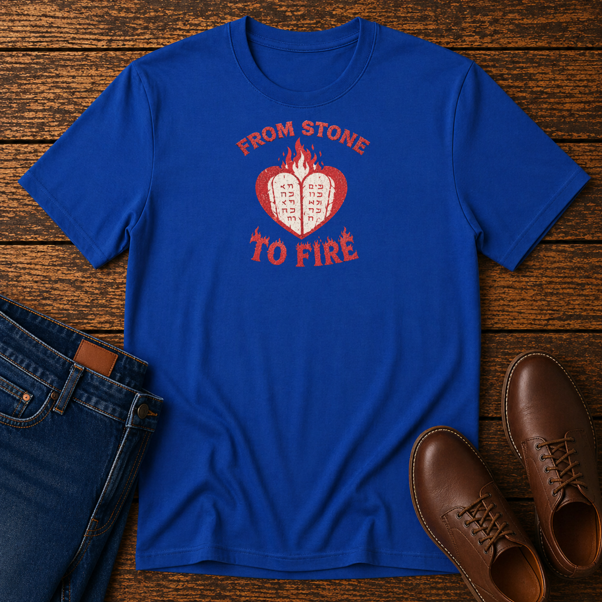 Royal blue From Stone to Fire tee with stone tablets in a flaming heart, laid flat with jeans and brown shoes