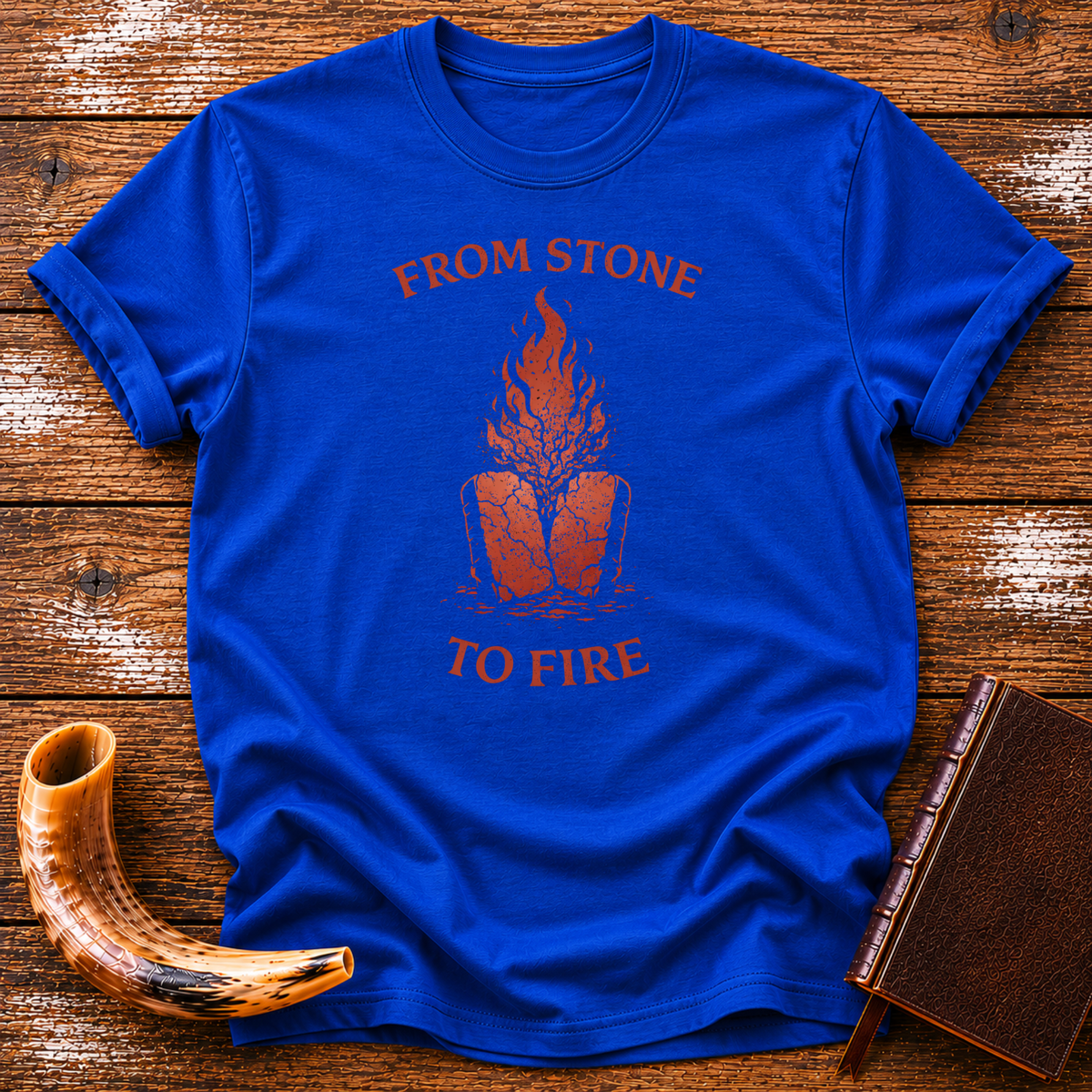 Royal blue From Stone to Fire tee with red flames rising from stone tablets, laid flat with a shofar and a leather-bound book
