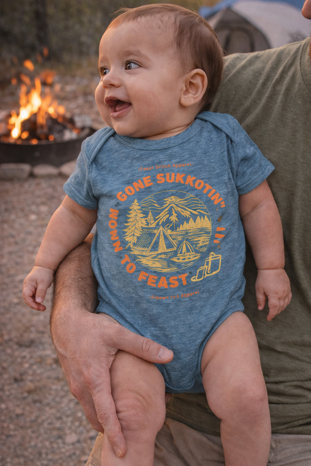 Vintage indigo Gone Sukkotin' Born to Feast baby bodysuit worn by a smiling baby held by an adult near a campfire