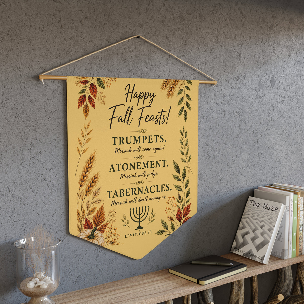 Happy Fall Feasts Leviticus 23 pennant with autumn leaves and wheat hanging above a bookshelf on a gray wall