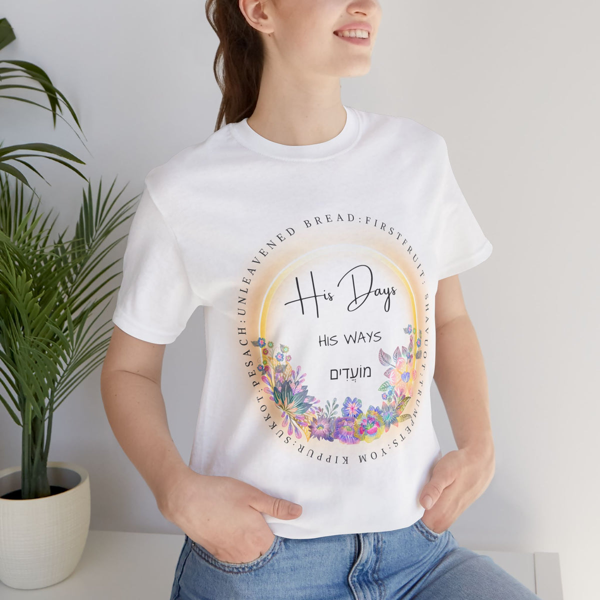 White His Days His Ways tee with a floral ring of feast names and Hebrew lettering, worn by a smiling woman