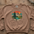 Espresso I Love Sukkot sweatshirt with a round mountain, pine tree and river camping scene, laid flat on a wooden table