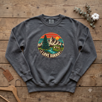 Pepper I Love Sukkot sweatshirt with a round mountain, pine tree and river camping scene, laid flat on a wooden table