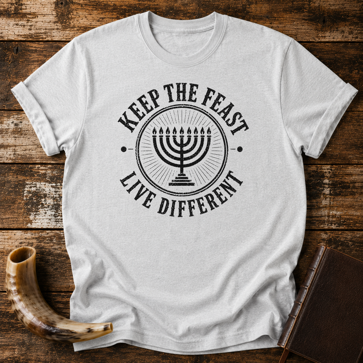 Sport grey t-shirt with a black seven-branch menorah inside KEEP THE FEAST LIVE DIFFERENT, laid flat with a shofar and a leather book