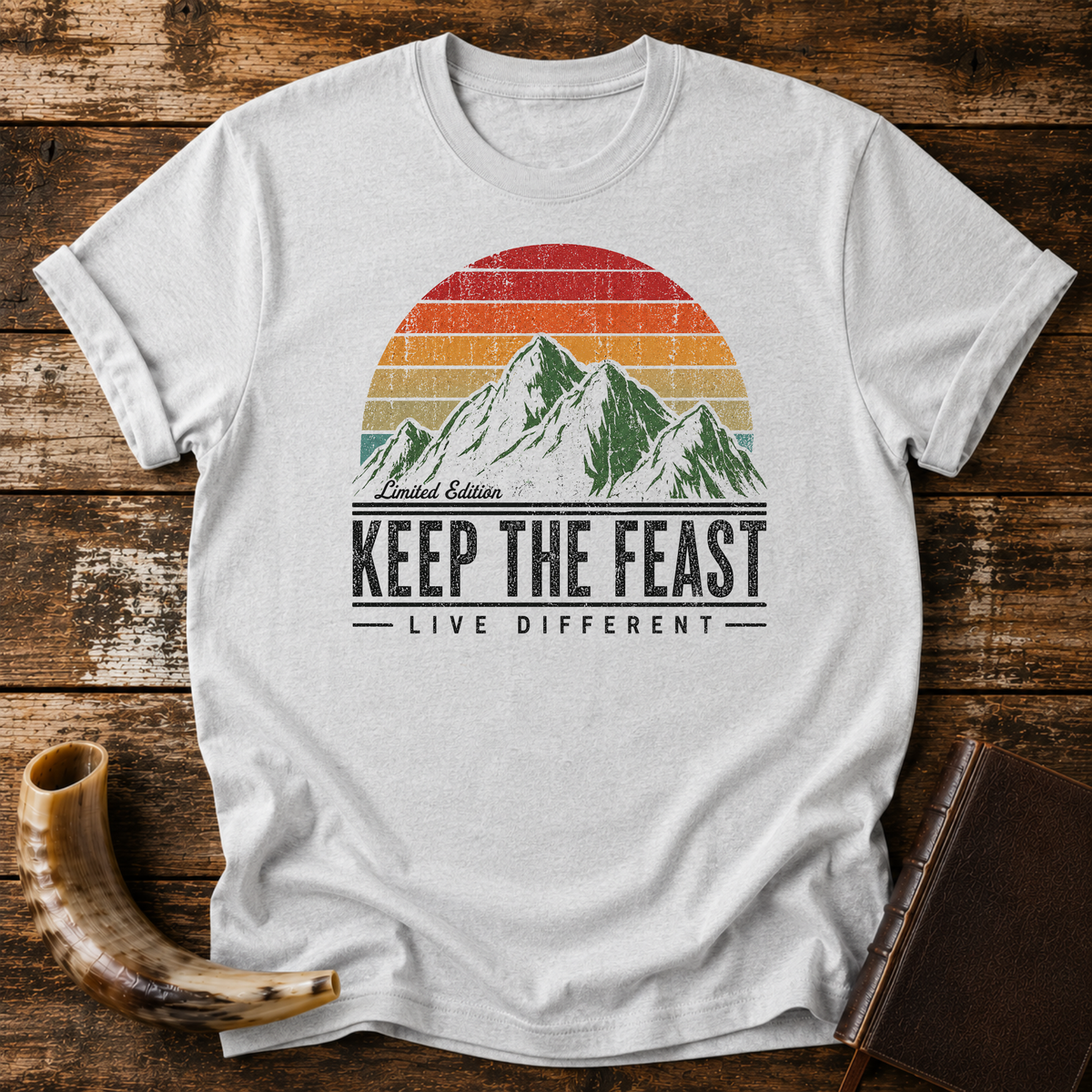 Sport grey t-shirt with Limited Edition KEEP THE FEAST LIVE DIFFERENT and a retro mountain sunset, laid flat with a shofar and a leather book
