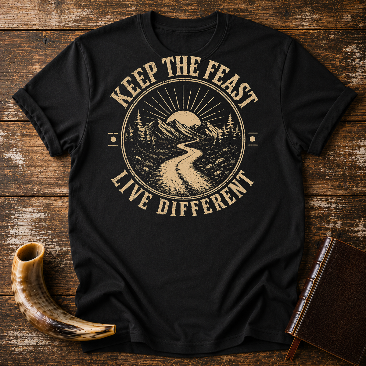 Black t-shirt with KEEP THE FEAST LIVE DIFFERENT around a winding road toward a rising sun, laid flat with a shofar and a leather book
