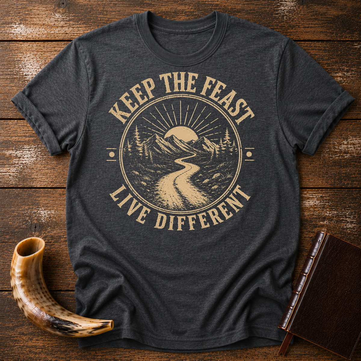Dark heather gray t-shirt with KEEP THE FEAST LIVE DIFFERENT around a winding road toward a rising sun, laid flat with a shofar and a leather book