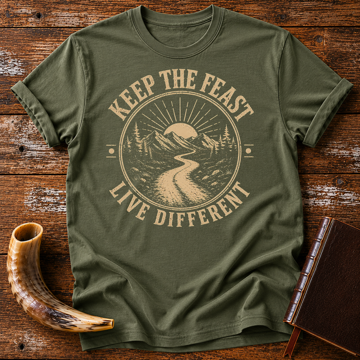 Military green t-shirt with KEEP THE FEAST LIVE DIFFERENT around a winding road toward a rising sun, laid flat with a shofar and a leather book
